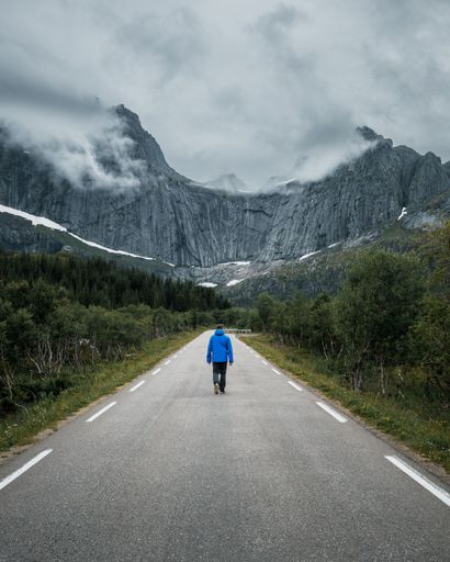 A vertical shot of a person walking on a road surrounded by rocky hills on a foggy day in winter