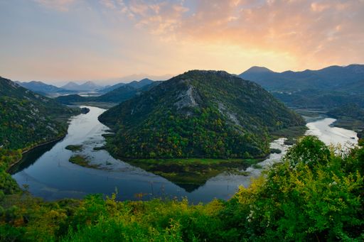 An aerial view of mountain landscape surrounded by dense trees and water during sunset