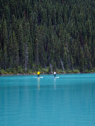 A vertical shot of Lake Louise in Banff National park, Canada, with two people paddle surfing