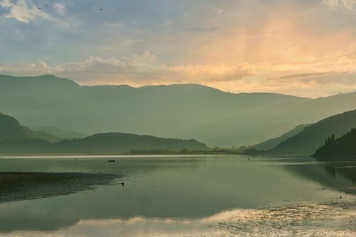A boat in Lake Skadar with high mountains and a cloudy pink sky in the background, Montenegro
