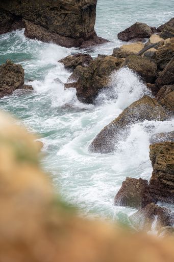 A vertical shot of foamy ocean waves hitting the big coastal rocks