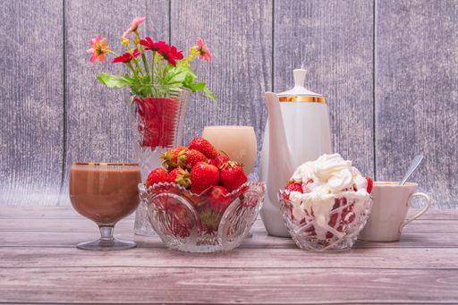 On wooden table there are vases with ripe strawberries, teapot, glasses and wine glasses with drinks. Still life with positive emotions.