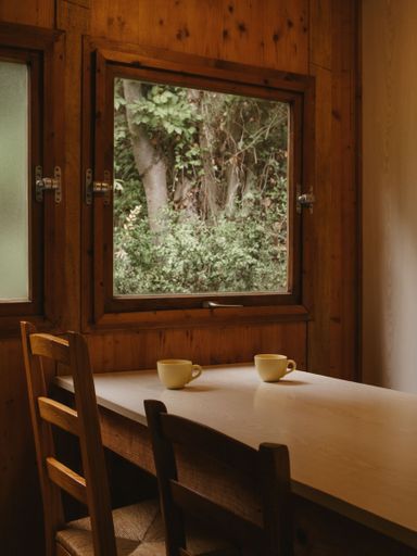 A vertical shot of a wooden table placed next to a window in a cozy environment