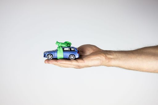 A closeup shot of a hand holding toy car with ribbon on the white background