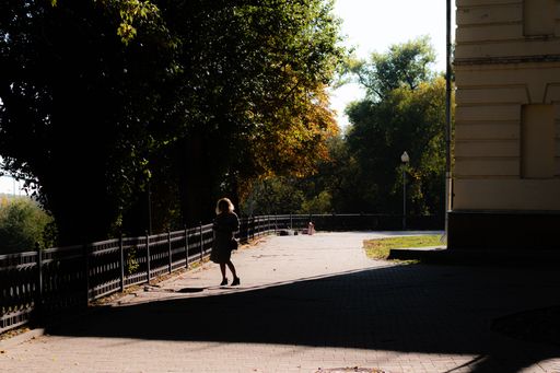 A woman walking on the sidewalk with trees in the background on a sunny autumn day