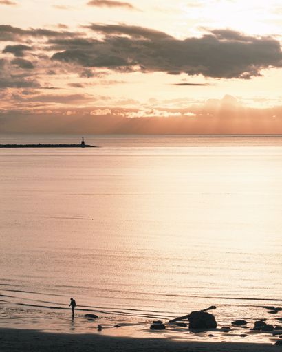 A vertical shot of a sea coast under a cloudy sky during sunset
