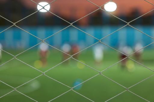 A blurred football net background and players behind the goal with blurred stadium and field pitch