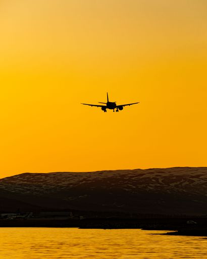 A silhouette of a plane flying over the water surface at sunset.
