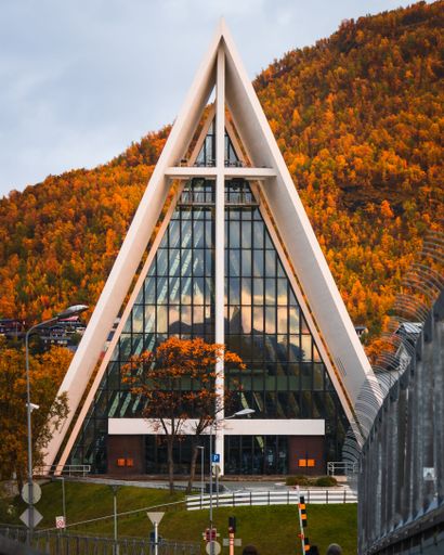 A vertical shot of the Arctic Cathedral in Tromso, Norway with autumn trees in the background