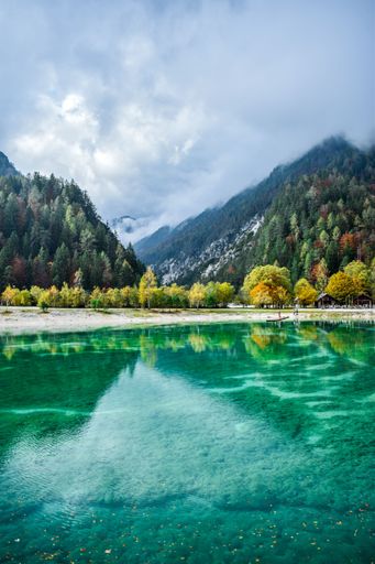 A vertical shot of blue lake with visible autumn tree reflections on a foggy day