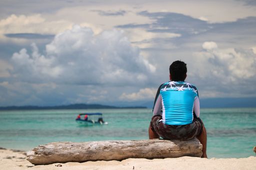 A Hispanic male sitting on a tropical beach and looking at the sea