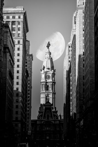 A grayscale shot of white half moon behind Philadelphia City Hall between tall buildings in Pennsylvania