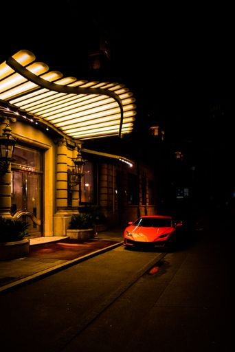 A vertical shot of a red Lamborghini parked in front of an illuminated hotel entrance at night