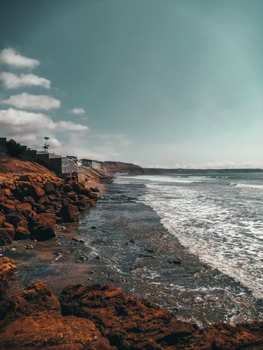 A beautiful view of calm sea on rocky coastline with buildings under blue cloudy sky