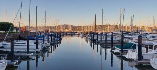 A panoramic shot of a port with moored boats and yachts under blue sky on sunny day
