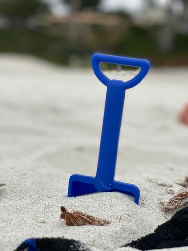 A vertical shot of a plastic toy shovel in sand on a beach