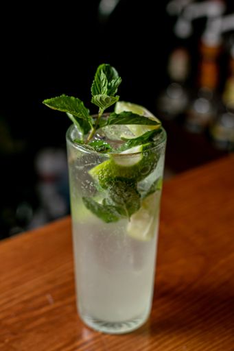 A glass of cool mojito with lime, lemon, ice, and mint leaves served on a bar counter