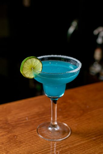 A glass of blue margarita with lime served on a bar counter
