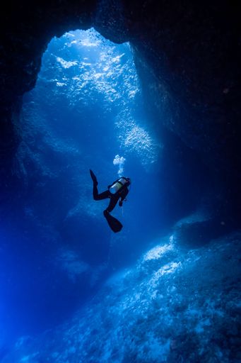 A vertical shot of a scuba diver swimming in an underwater cave near to the surface