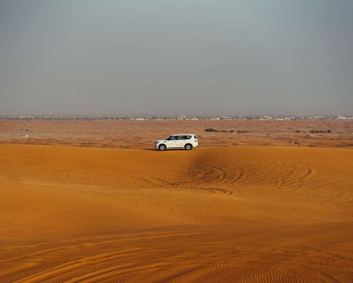 A white jeep parked on a brown sandy hill in a dessert on a sunny day