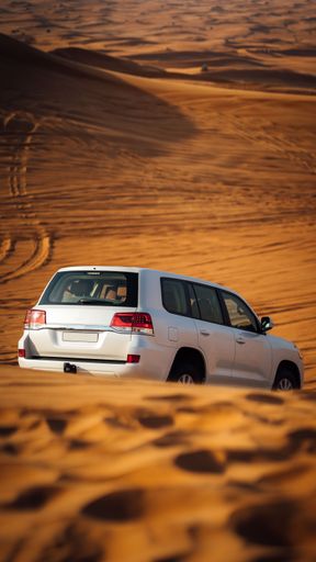 A vertical closeup of a silver Jeep driving on the sand in a yellow dessert on a sunny day