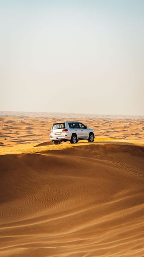 A vertical shot of a silver Jeep parked on a sandy hill in a dessert on a sunny day