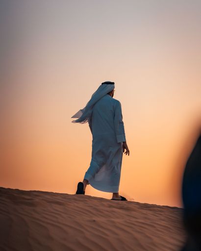A vertical shot of a man walking on the sand in a desert in Dubai, United Arab Emirates