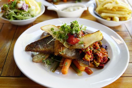 A closeup of a delicious dish with fish and vegetables on a white plate