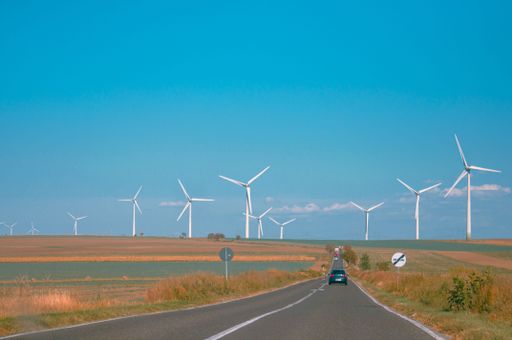 A landscape shot of a countryside road against a background of wind turbines under the clear blue sky