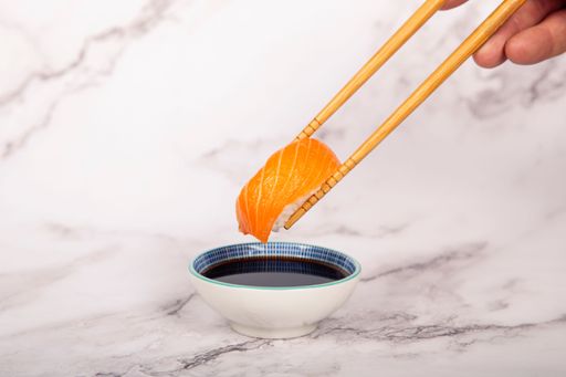 A close-up shot of a hand holding chopsticks with salmon nigiri over soy sauce