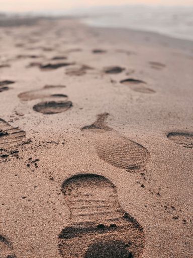 A vertical closeup of a wet sand on the beach with lots of footsteps, blurred background