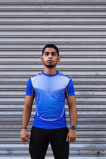 A vertical shot of a young Hispanic male standing straight in front of a garage door