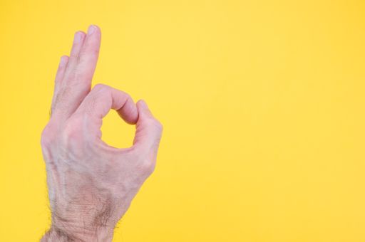 detail of male hand doing OK gesture on a yellow background