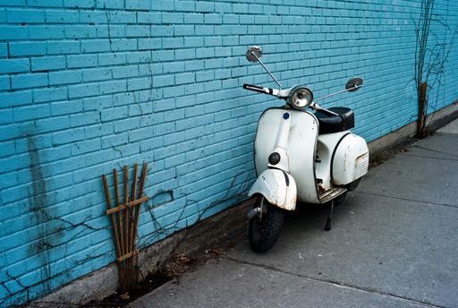 Old-fashioned scooter in front of a blue brick wall in a city street.
