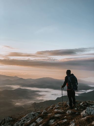A vertical shot of a hiker admiring the view with a waterscape and a mountain range