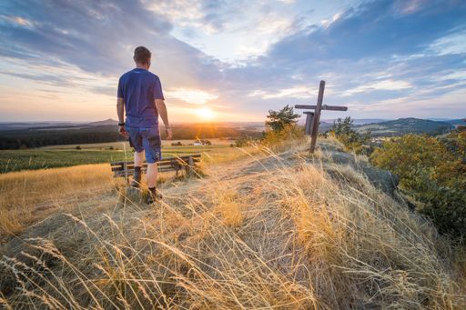 A man enjoying the view of the sunset standing on a hill at a field