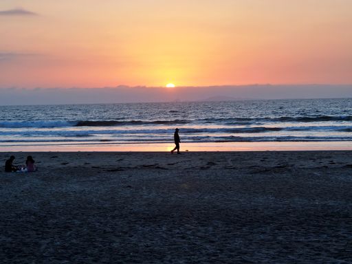 A silhouette of a man walking on the beach during pink sunset