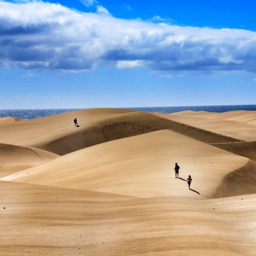 A group of people walking over sand dunes under a cloudy sky