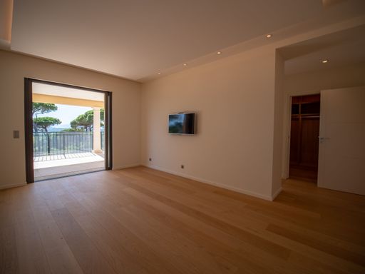 An empty room with a wooden floor, beige walls, a balcony and a corridor to the right