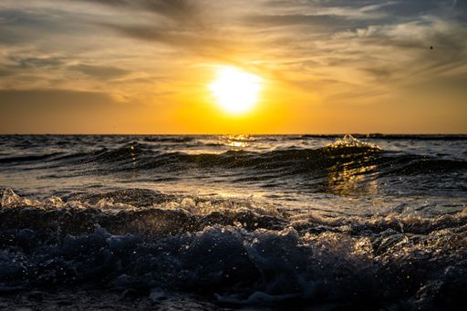 A beautiful sunset over the ocean with a yellow horizon and tidal waves crashing the shore