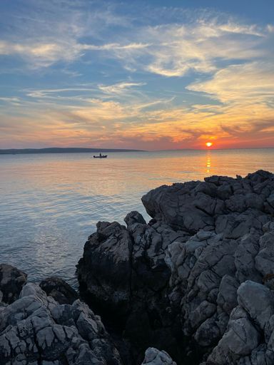 A vertical shot of the sea at sunset with a boat silhouette in the background