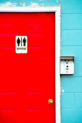 Male and female signs on red wooden restroom door of blue stone building