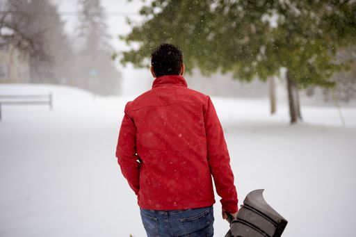A closeup shot from behind of a male wearing a red jacket and holding a snow shovel with a blurred background