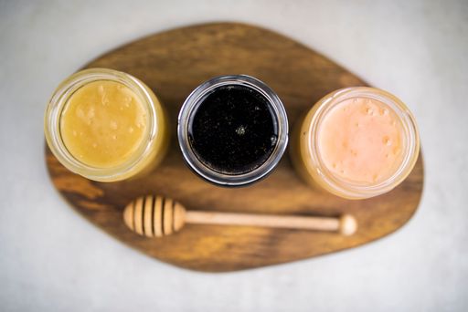 The three jars of honey, jams on the wooden table, and a honey dipper, top view