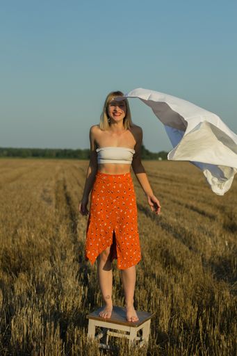 A vertical shot of a female model standing on a chair in a field with a rippling bedsheet