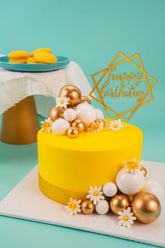 A yellow birthday cake decorated with balls in different colors and shapes