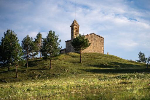 The Santuari de Santa Maria del Puig-aguilar on top of a green heel under the cloudy sky