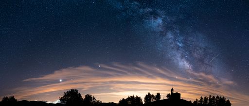 A scenic panoramic view of the silhouettes of a Sanctuary and trees under the starry night sky