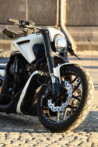 A vertical closeup of a white chopper motorcycle parked under the sunlight