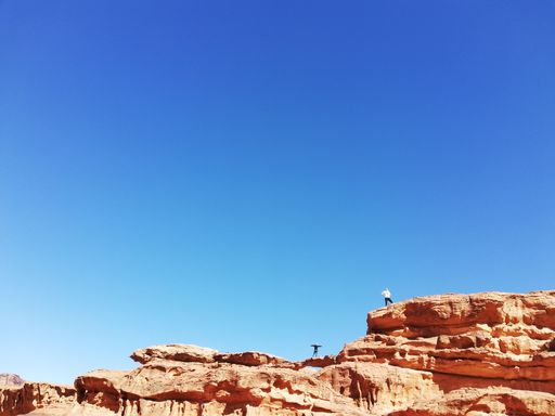 A low angle shot of two people on top of cliff with a clear blue sky on the background